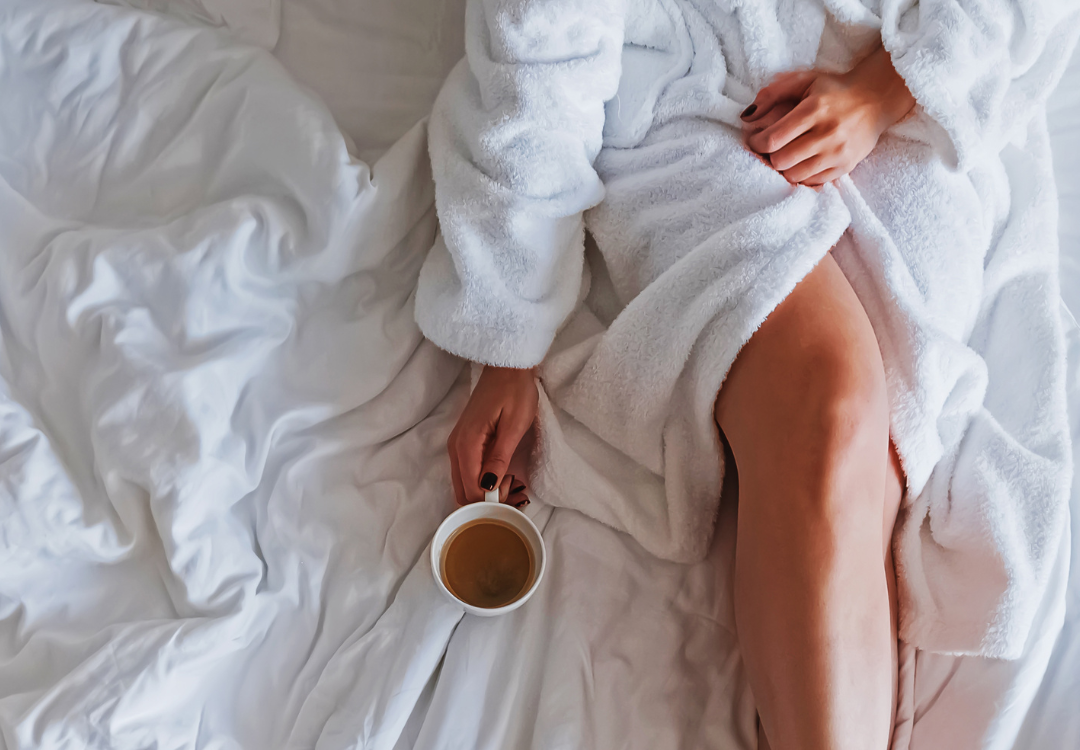 Woman sitting in bed with a rob on and holding a mug with tea