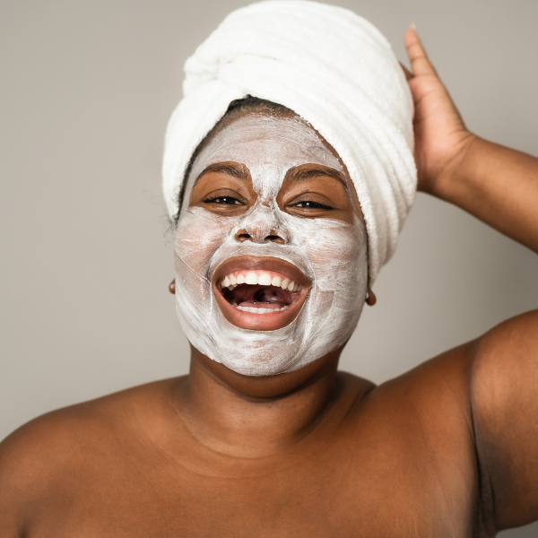 Woman smiling with a skincare face mask and towel on her head.