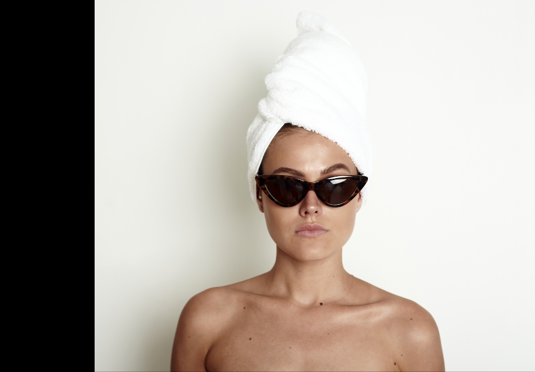 Woman with a straight face wearing a towel on her head and dark sunglasses.