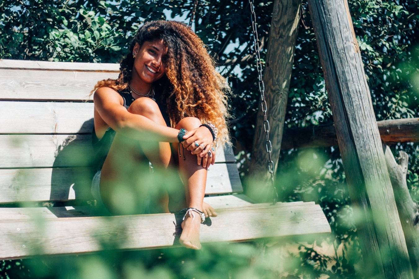 Woman smiling while sitting on a swing bench and holding her legs.