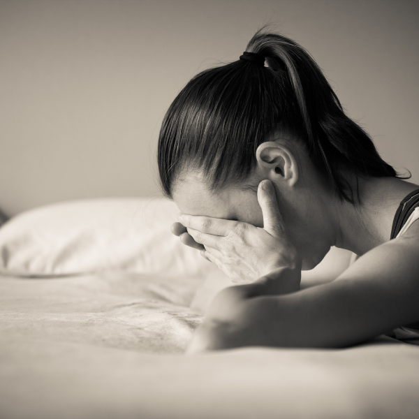Black and white image of a woman leaning on a bed while holding her face in her hands because she's feeling stressed and anxious..