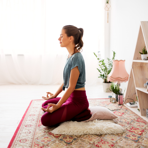 Woman practicing self-care and meditating while sitting on pillows in a pink decorated room.