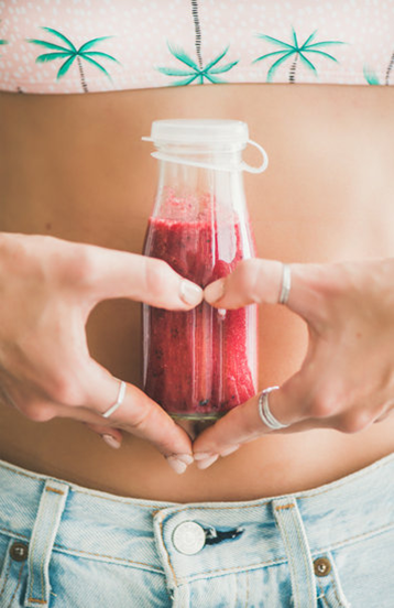 Woman holding a juice cleanse with her hands and fingers shaped into a heart.