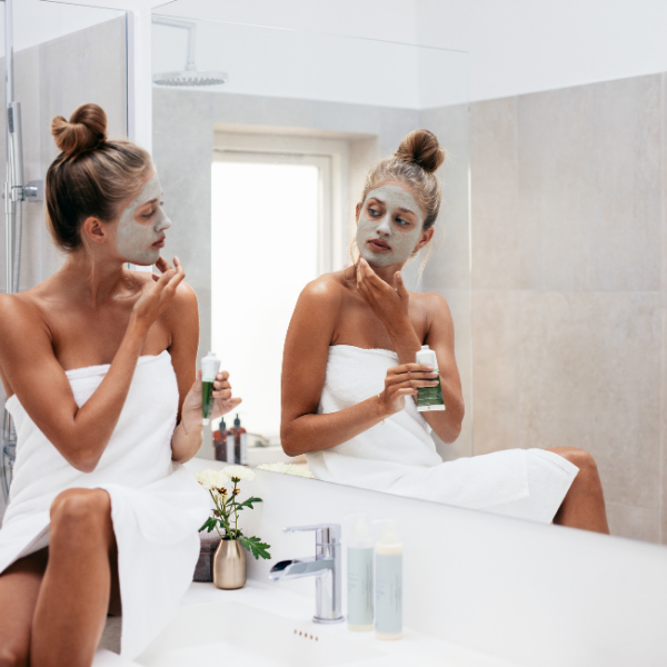 Woman looking in a mirror applying a face mask while giving herself a facial at home.
