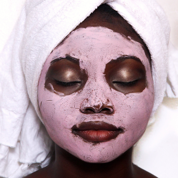 Close up image of a woman wearing a towel on her head, with a pink skincare face mask
