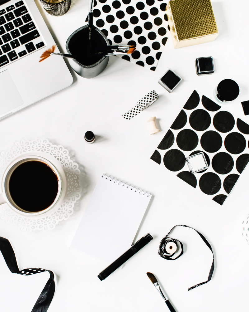 A table with various black and white items such as a laptop, coffee mug, pens, and note pads.