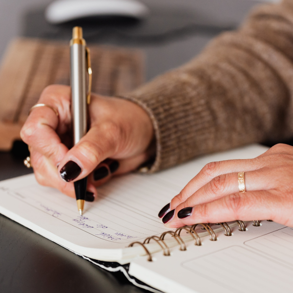 Woman with black fingernail polish writing in a journal.