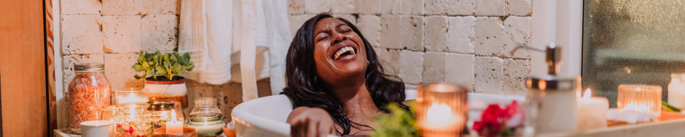 Woman smiling while in a bathtub surrounded by candles.