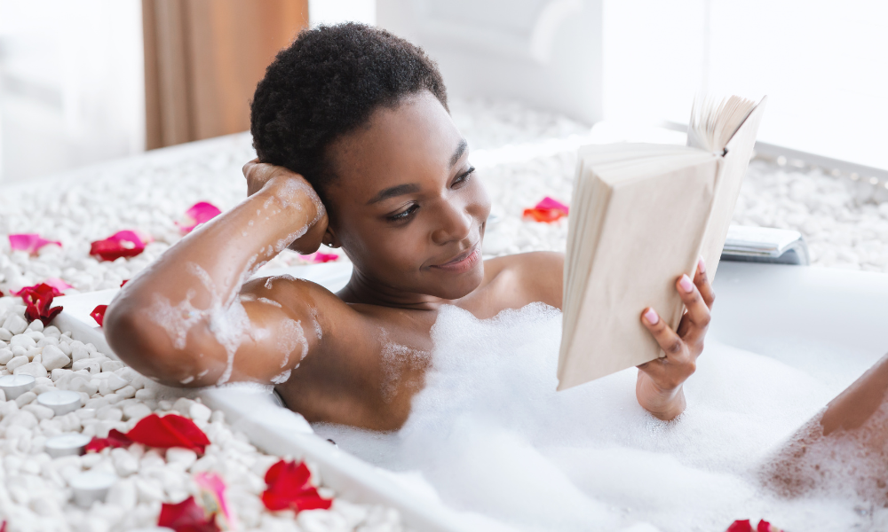 Woman in bubble bath surrounded by flowers while reading a journal.