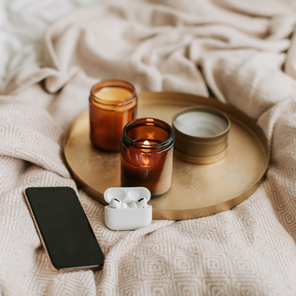 Candles, cell phone, and headphones laying on a blanket.