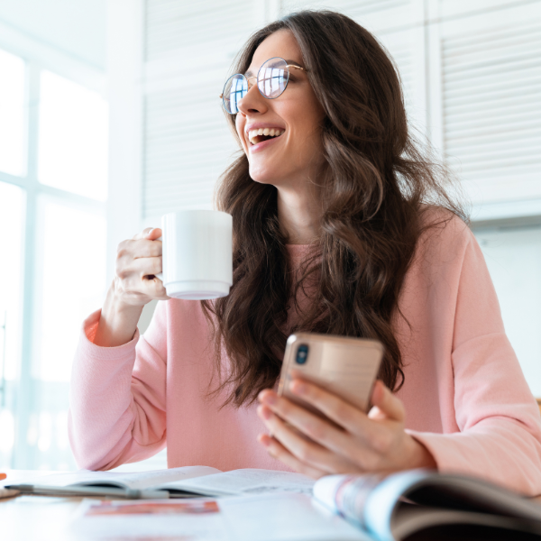 Woman smiling while holding a mug and a cell phone